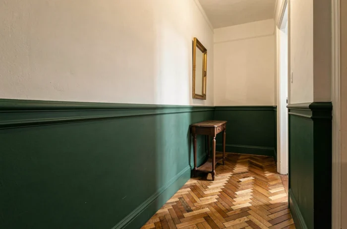 Soubassement peint en vert forêt avec haut de mur blanc cassé créant un contraste bicolore dans un couloir avec parquet en chevron et console
